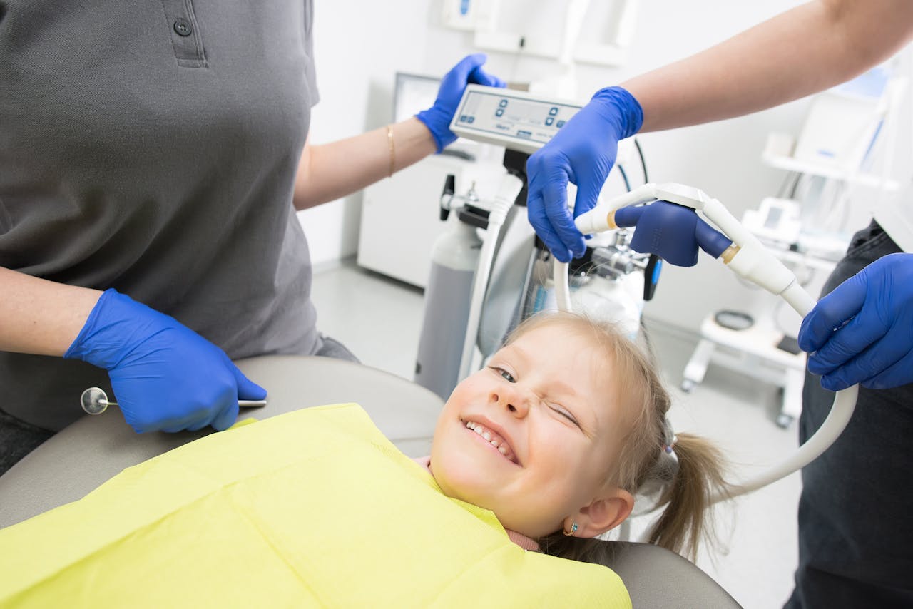 The Art of Drawing Readers In: Your attractive post title goes here A cheerful child winks while sitting in a dental chair, surrounded by dental professionals.